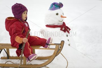 Young girl playing on a sledge near a snowman