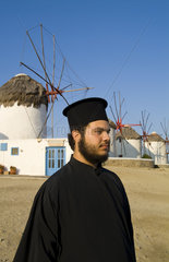 Beautiful scenic color of white famous windmills on beach with Greek Orthodox priest of beautiful island of Mykonos Greece