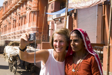 Tourist woman taking self portrait with Hindu woman in front of the Wind Palace in downtown center of the Pink City of Jaipur in Rajasthan India