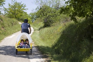 Two children in a sleigh pulled by a bicycle
