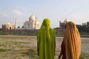 World famous Taj Mahal temple burial site at sunset with women in sari from Yamuna River with reflection in town of Agra India