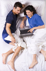 Dating couple happy together on internet computer even in bed perhaps addicted to computer