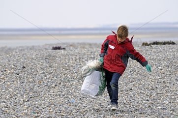 Kind mit einem Müllsack auf einem Kieselstrand trägt