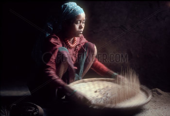 NEPAL : Terai  the lowlands bordering India. In a village near Meghauli. A Tharu woman is winnowing rice in her home.