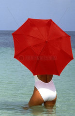 Woman in Caribbean with graphic red umbrella in water of ocean relaxing and unwinding