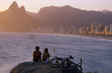 Couple at Arpoador stones  enjoying the sunset at Ipanema beach  Rio de Janeiro  Brazil.