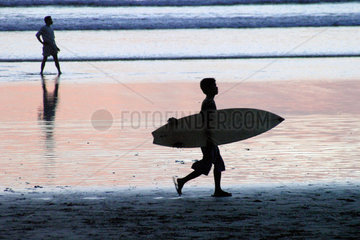 Indonesia: South-West coast of Bali  Legian.Young local surfer walks with his board under his arm.