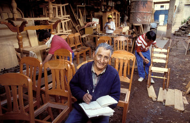 Peru  Cusco; Manager doing his administration in the carpentry workshop of his furniture factory. Two men are working on wooden chairs.