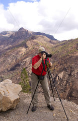 Photographer with tripod taking pictures of remote cliffs of Gran Canaria with mountains near National Nablo in La Cumbre or Cumbre region in Canary Islands Spain