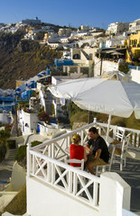 Santorini Greece and the beautiful white buildings on the mountain cliffs of main city of Fira and romantic couple relaxing on terrace