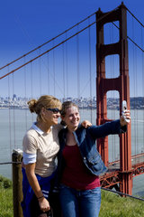 Tourists enjoying sunshine and taking portrait picture of Famous Landmark of San Francisco the Golden Gate Bridge and the bay and city behind