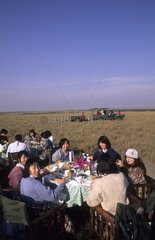Japanese tourists in middle of safari in jungle having breakfast after balloon ride in Kenya Africa