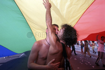 Rio de Janeiro  Brazil. Gay parade. Racial-mixed gay couple in love under the multi-colored gay flag. Kiss.