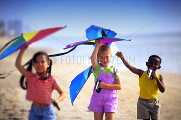 Mixed ethnic children playing on beach flying kites having fun together