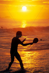 Sport and fun at Ipanema beach  Rio de Janeiro  Brazil. Young man plays frescobol. Tropical beach  recreation  sunset  diversion  amusement  racket  racquet and ball