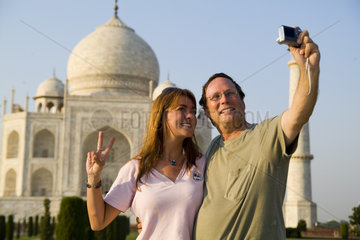 Tourist couple in their 40s taking self portrait with camera on holiday in front of the famous Taj Mahal one of the wonders of the world in Agra India