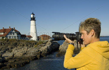 Tourist taking photograph at the famous Portland Head Light lighthouse in Portland Maine in bright sunshine sunny day