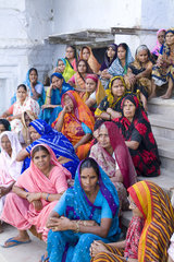 Colorful Hindu women in costumes and veils sitting on the steps waiting for boat in the religious village of Mathura India