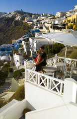 Santorini Greece and the beautiful white buildings on the mountain cliffs of main city of Fira and romantic couple relaxing on terrace