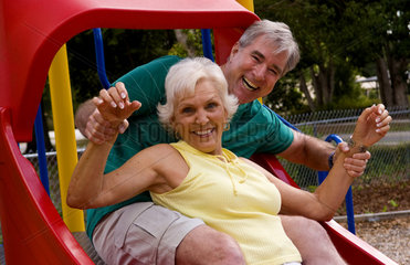 Senior retired couple having fun at playground outside with slide