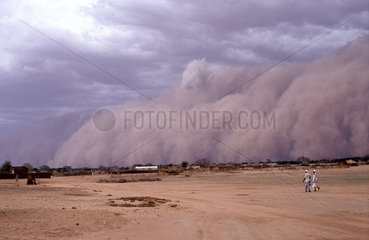 Sudan  Nfala. Sandstorm approaching a village. People walking in front.