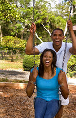Black African American couple dating and playing on swing at playground