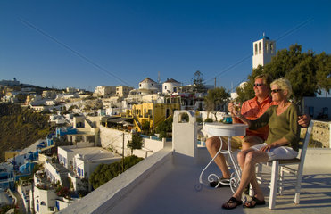 Santorini Greece and the beautiful white buildings on the mountain cliffs of main city of Fira and retired couple relaxing on terrace
