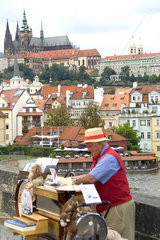 Colorful vendor on famous Charles Bridge with syncopator music with Castle District in background of tourist city of Prague in Czech Republic