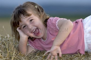 Smiling young girl lengthened on a ball of straw