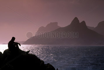 Sunset at Ipanema beach  Rio de Janeiro  Brazil. Pensive  thoughtful man sitted in the Arpoador Stones.