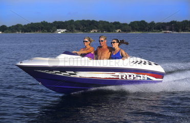 Couples running motor boat with wake and excitement as it moves thru water with speed