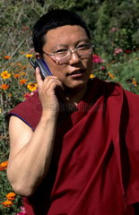 Male monk Buddhist in red gown on cell phone in rural Tibet China