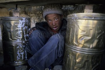 Young Tibetan sitting between two prayer rollers China