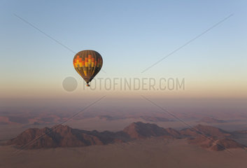 The hot-air balloon above an arid plain and isolated mountain ridges at the edge of the Namib Desert. Aerial view from a second balloon. NamibRand Nature Reserve  Namibia.