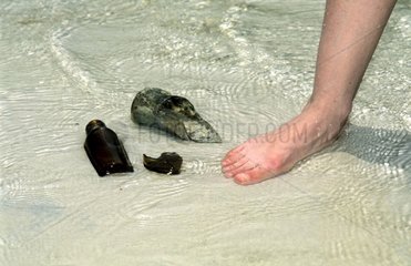 Pied d'un baigneur et tessons de bouteilles sur du sable