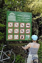 Woman on a bicycle reading a panel of Natural Reserve France