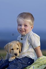 Kleiner Junge mit einem Labrador -Welpen in den Armen sitzt