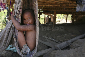 Closeup of Burmese boy sitting in a hammock tied to a hut in the displaced persons camp near Thailand. In Myanmar (Burma)  thousands of people have settled near the border as a result of oppression in their homeland. Around 200 Burmese displaced people ha