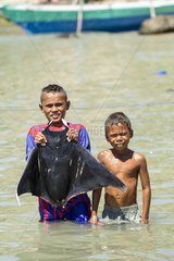 Boy handling mobula ray in water - Solor Indonesia