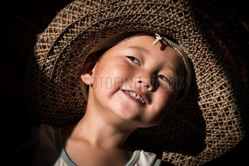 Young Kyrgyz child  with my hat lit by the sunlight in front of the door of a yurt.