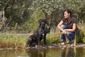 Black Cane Corso and woman sitting at the water's edge