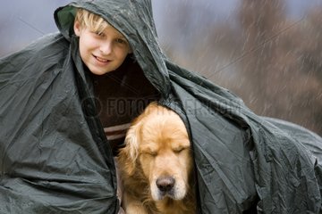 Boy with dog under a cape of rain during a downpour