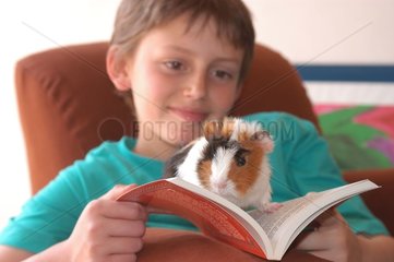 Enfant lisant avec son cochon d'Inde tricolore