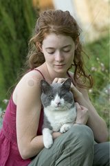 Young red-haired girl caressing a cat in the garden