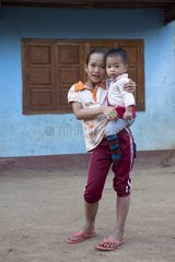 Girl carrying a baby in front of a blue house in Laos