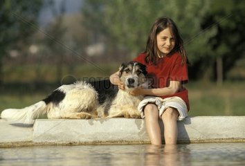 Fille assise avec un chien bâtard au bord d'un bassin