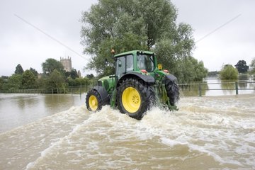 Green tractor driven on a flooded road in Tewkesbury UK