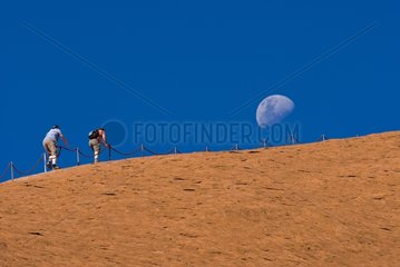Two climbers scrambling up the slopes of Uluru with moon