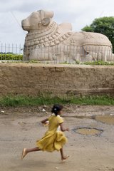 Child running in front of the statue of the god Lepakshi Nandi India