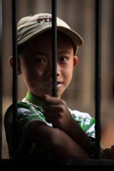 Young boy behind the bars of a window in Burma